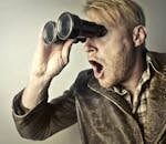A surprised man in a leather jacket peers through binoculars with a shocked expression.