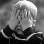 Anti Flüchtling? A black and white photo of a child covering their face, capturing a moment of play or reflection.