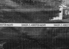 Black and white photo of an asbestos hazard warning sign on a fence.
